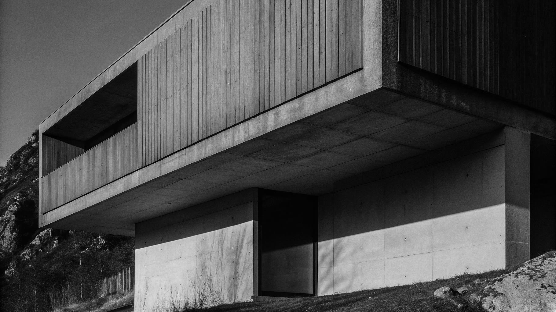 Casa in calcestruzzo a sbalzo su un pendio, in bianco e nero, con ombre nette